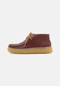 Brown leather shoes with a rounded toe, stitched detailing, and a thick, textured rubber sole. Features light brown laces and contrasting accents.