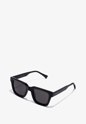 Occhiali da sole neri in plastica con forma quadrata, lenti scure e stanghette sottili. Presentano un'elegante marca dorata su un'asta.