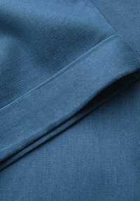 Tissu bleu plié pour montrer un motif en maille texturée et un détail d'ourlet cousu en gros plan.