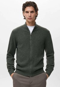 Maglione a coste verde scuro con collo zip, maniche lunghe e polsini aderenti. Realizzato in materiale morbido, ha una texture liscia e un design aerodinamico.