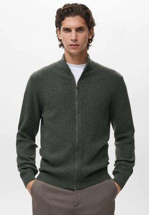Jersey de color verde oscuro con cuello con cremallera, mangas largas y puños ajustados. Confeccionado en un material suave, tiene una textura lisa y un diseño aerodinámico.