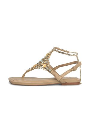 Sandalia plana beige con adornos de pedrería y gemas, tira en el tobillo con hebilla y cadena decorativa en el talón.