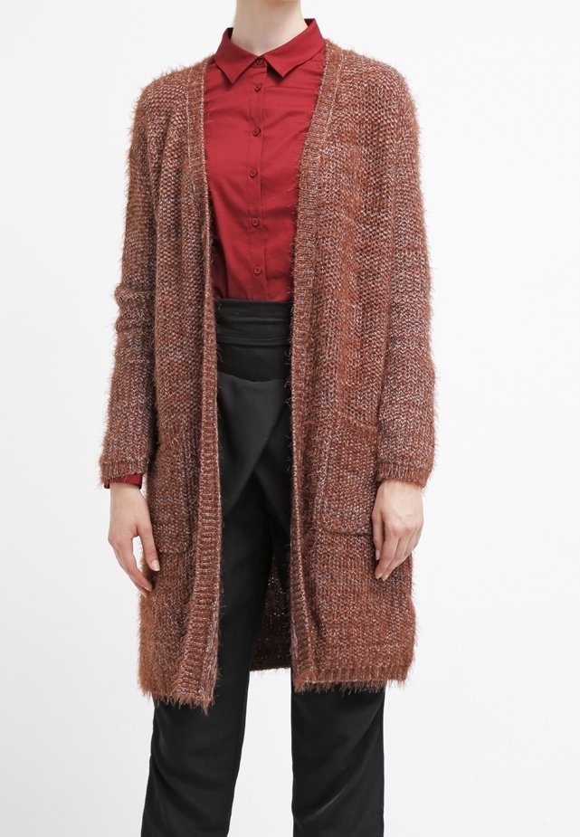 Lång, öppen kofta i ett texturerat, mjukt brunt material med två framfickor, bärs över en röd skjorta med krage och svarta byxor.