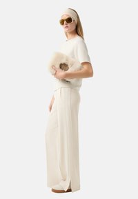 Lichtbeige top en wijde broek, aangevuld met een bonten clutch en oversized zonnebril, met een zachte textuur en subtiele details.