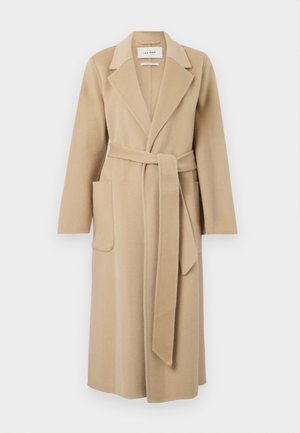 Lange beige wollen jas met brede revers, twee voorzakken en een bijpassende riem die in de taille is gestrikt.