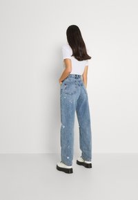 Jeans azzurri chiari a vita alta con una vestibilità rilassata, caratterizzati da un lavaggio sbiadito e dettagli strappati. Abbinati a stivali bianchi con piattaforma.