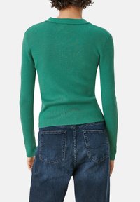 Grüner gerippter Pullover mit langen Ärmeln und Kragen, kombiniert mit dunkelblauen Jeans aus Denim mit Gesäßtaschen und geradem Schnitt.