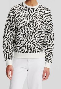 Musta-valkoinen collegetakki siksak-kuviolla, resorilla varustetulla pyöreällä kaula-aukolla ja hihansuilla, rento istuvuus ja teksturoitu kangas.