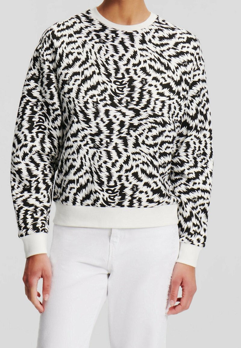 Musta-valkoinen collegetakki siksak-kuviolla, resorilla varustetulla pyöreällä kaula-aukolla ja hihansuilla, rento istuvuus ja teksturoitu kangas.