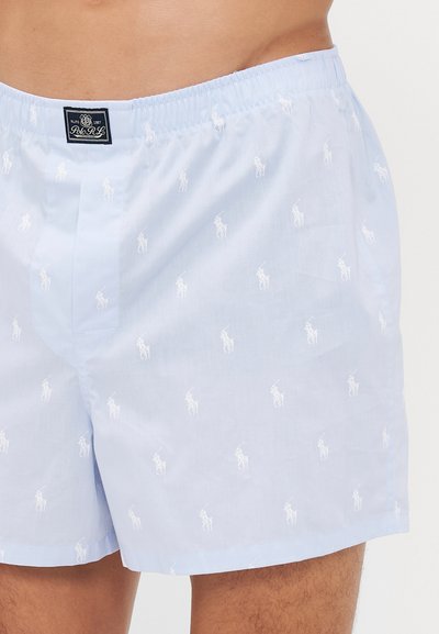 Svjetloplave muške bokserice s bijelim izvezenim Polo Ralph Lauren logotipima i elastičnom trakom u struku koje nosi osoba.