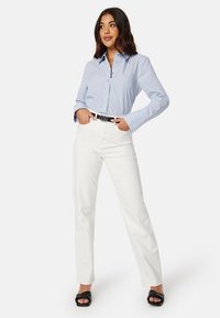 Blauw-wit gestreepte button-down shirt, gecombineerd met witte rechte broek, zwarte riem en zwarte open-toe slides.