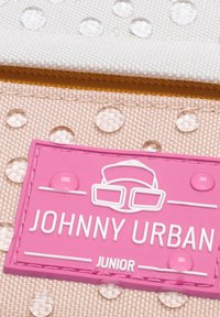 Rózsaszín textil címke domború "JOHNNY URBAN JUNIOR" felirattal, textúrált, pöttyös háttérrel, vízcseppekkel.
