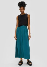 Zwarte mouwloze top van textuurstof, gecombineerd met een vloeiende teal maxi rok met elastische tailleband, gedragen met zwarte platform sandalen.