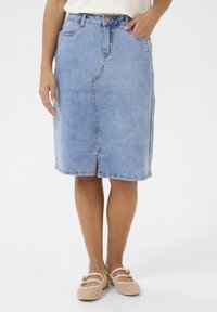 Světle modrá džínová sukně ke kolenům, se spodničkou, poutky na pásek a standardními kapsami. Spárována s béžovými plochými botami.