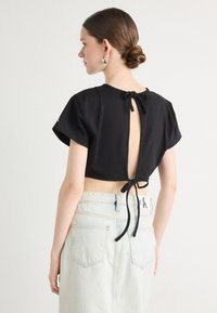 Fekete, rövid ujjú, crop top hátsó megkötővel és nyitott dizájnnal. Fényes mosott farmer szoknyával párosítva, hátul zsebekkel.