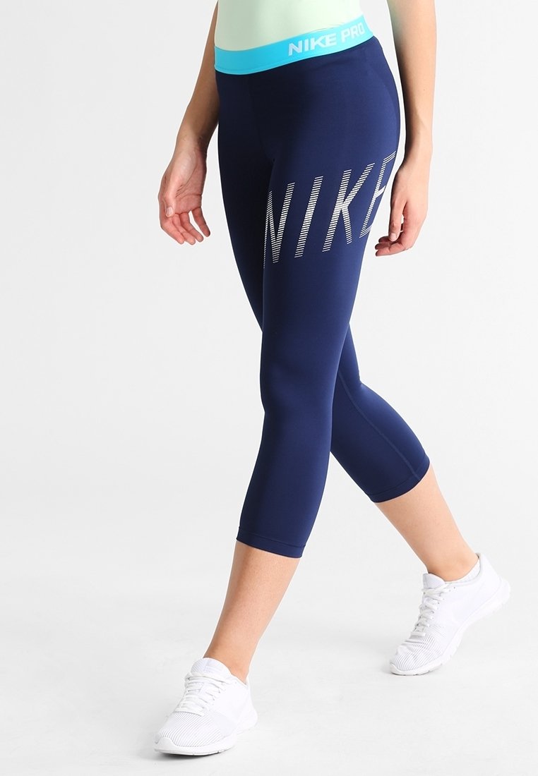 Granatowe legginsy capri wykonane z gładkiego, elastycznego materiału. Posiadają wyraźne srebrne logo "NIKE" oraz turkusowy pas.