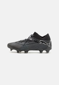 Svart fotbollssko med en texturerad ovandel, svarta snören och en distinkt vit Puma-logotyp på sidan. Utrustad med flera dobbar för bättre grepp.