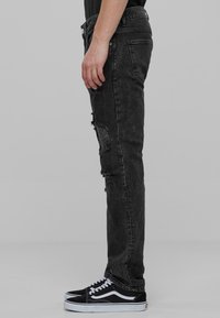 Mustat kuluneet farkut, joissa on repeämiä edessä, slim fit -tyyli ja hieman haalistunut pinta. Yhdistetty mustiin tennareihin, joissa on valkoisia yksityiskohtia.