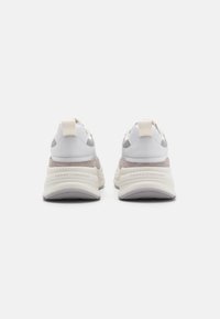 Zapatillas blancas y grises con un panel de ante texturizado, una suela gruesa y una lengüeta de tela en el talón. Logo de la marca grabado en el talón.
