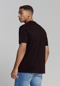 Zwarte poloshirt met kraag, korte mouwen en een relaxed fit; gedragen met lichtblauwe spijkerbroeken. Zichtbare stiksels op de mouwen.