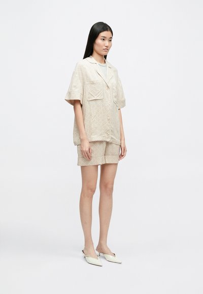 Béžová polokošele s krátkym rukávom a dvoma vreckami, skombinovaná s ladiacimi šortkami. Hladká textura a jemný diamantový vzor. Biele špicaté balerínky.