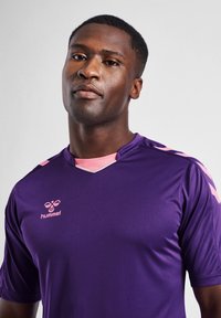 Purple sports jersey with short sleeves, featuring pink accents on the shoulders and neckline. "Hummel" logo in pink on the chest.