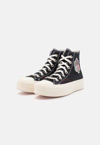 Schwarze High-Top-Sneaker aus Canvas mit weißen Schnürsenkeln, Gummisohlen und gesticktem Blumenmotiv auf der Außenseite.