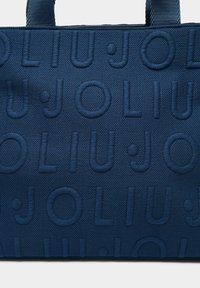 Tumesinist värvi käekott, millel on reljeefne logomuster. Valmistatud tekstuurse materjaliga, millel on kaks vastupidavat kandemehhanismi.