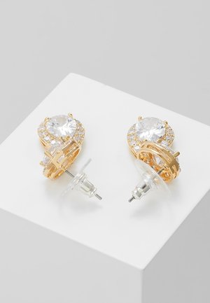 Boucles d'oreilles clous couleur or avec de gros cristaux clairs en forme de larme entourés de petits cristaux ronds, fixées par des attaches en plastique transparent.