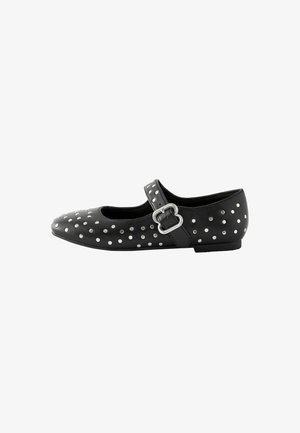 Chaussure Mary Jane en cuir noir avec des clous argentés, bout rond et une sangle à boucle sur le côté. Semelle plate avec une finition texturée.