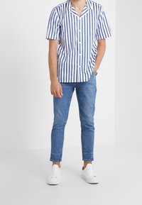 Raitainen lyhythihainen paita valkoisena ja sinisenä, yhdistetty vaaleansinisien kapeiden farkkujen ja valkoisten tennarien kanssa. Edessä napillinen ja siinä on kaulus.