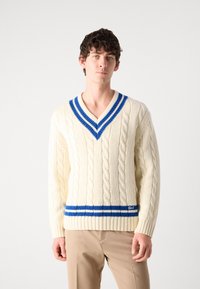 Maglione color crema a maglia cablè con scollo a V, caratterizzato da dettagli a righe blu sul colletto e sull'orlo. Maniche a costine e vestibilità casual.