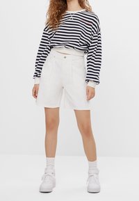 Felpa a righe navy e bianca con maniche lunghe, abbinata a pantaloni corti bianchi a vita alta. Completato con sneakers bianche.