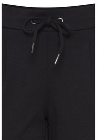 Pantalon de survêtement noir en gros plan montrant un cordon noué avec des embouts métalliques et des détails sur la couture avant.
