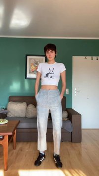 White cropped T-shirt with a black rabbit print, light plaid trousers with side pockets, and black athletic shoes. Brown sofa in background.