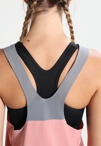 Sport tanktop med et sort og gråt lagdelt design og en pink nederste sektion, der fremhæver en racerback-skæring og blødt, tekstureret stof.