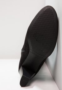 Scarpa in suede nera con suola in gomma texturizzata. Presenta una punta arrotondata e un tacco sottile. Taglia 37 indicata sulla parte inferiore.