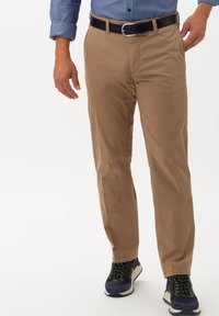 Chino in cotone color beige con vestibilità dritta, dotati di una cintura nera e abbinati a sneakers blu navy con dettagli verdi.