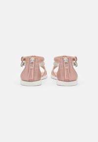 Sandalias sintéticas rosas con cremalleras traseras, acentos en blanco, lados abiertos y una suela de goma blanca. Diseño de zapato plano para uso casual.