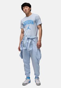 T-shirt in cotone azzurro chiaro con testo e logo "JORDAN"; pantaloni della tuta azzurri chiari abbinati; sneakers bianche con dettagli grigi; abbigliamento sportivo casual.