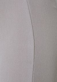 Ljusgrått texturerat tyg som visar ribbade och släta sektioner, med synlig sömnad. Har en subtil lyster och varierande ytmönster.