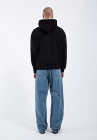 Black hooded sweatshirt with a relaxed fit, paired with light blue loose-fit jeans featuring back pockets and a faded texture.