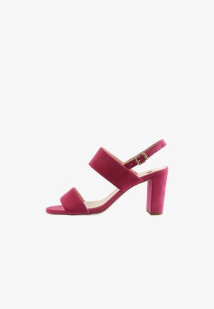 Różowy zamszowy damski sandał na wysokim obcasie z dwoma szerokimi paskami i regulowanym paskiem wokół kostki na białym tle.