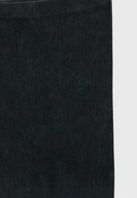 Tissu noir côtelé, présentant des lignes verticales avec une texture douce. Le bord est fini avec soin, mettant en valeur une silhouette lisse.