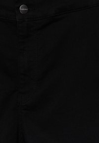 Tissu en denim noir avec des surpiqûres visibles et un bouton métallique gravé « Pull&Bear » sur la ceinture.