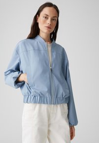 Veste bomber bleu clair avec fermeture éclair à l'avant, taille élastique et poches latérales. Tissu texturé avec une coupe décontractée et des épaules tombantes.