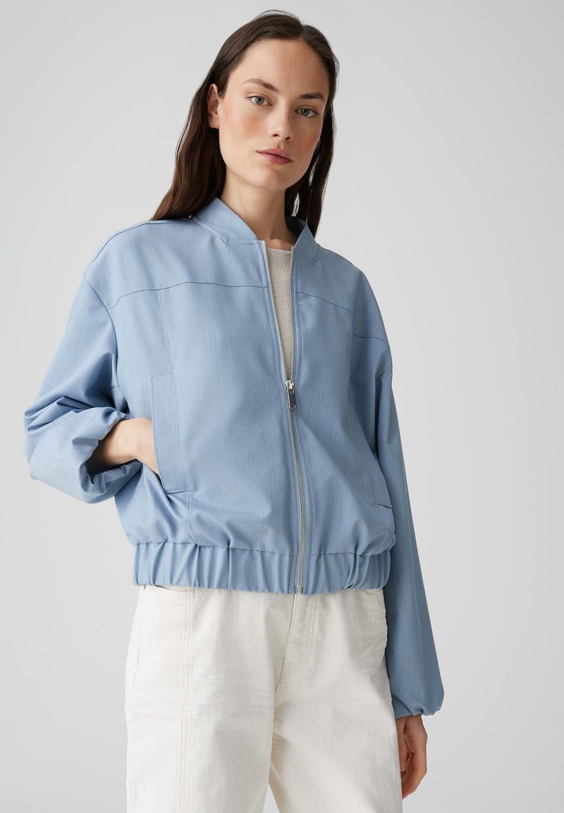 Veste bomber bleu clair avec fermeture éclair à l'avant, taille élastique et poches latérales. Tissu texturé avec une coupe décontractée et des épaules tombantes.