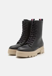 Czarne skórzane botki za kostkę o fakturowanym wykończeniu, z grubą beżową podeszwą i czarnymi sznurówkami. Kolorami akcentującymi są czerwony i niebieski na pięcie.