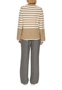 Beige- und weiß gestreifter Pullover mit langen Ärmeln und hohem Kragen, kombiniert mit grauen weiten Hosen. Engmaschige Textur, lässiges Design.