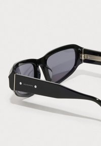 Μαύρα ορθογώνια γυαλιά ηλίου με σκούρους φακούς και φαρδιές βραχίονες, με το λογότυπο της μάρκας AllSaints πάνω στον βραχίονα.